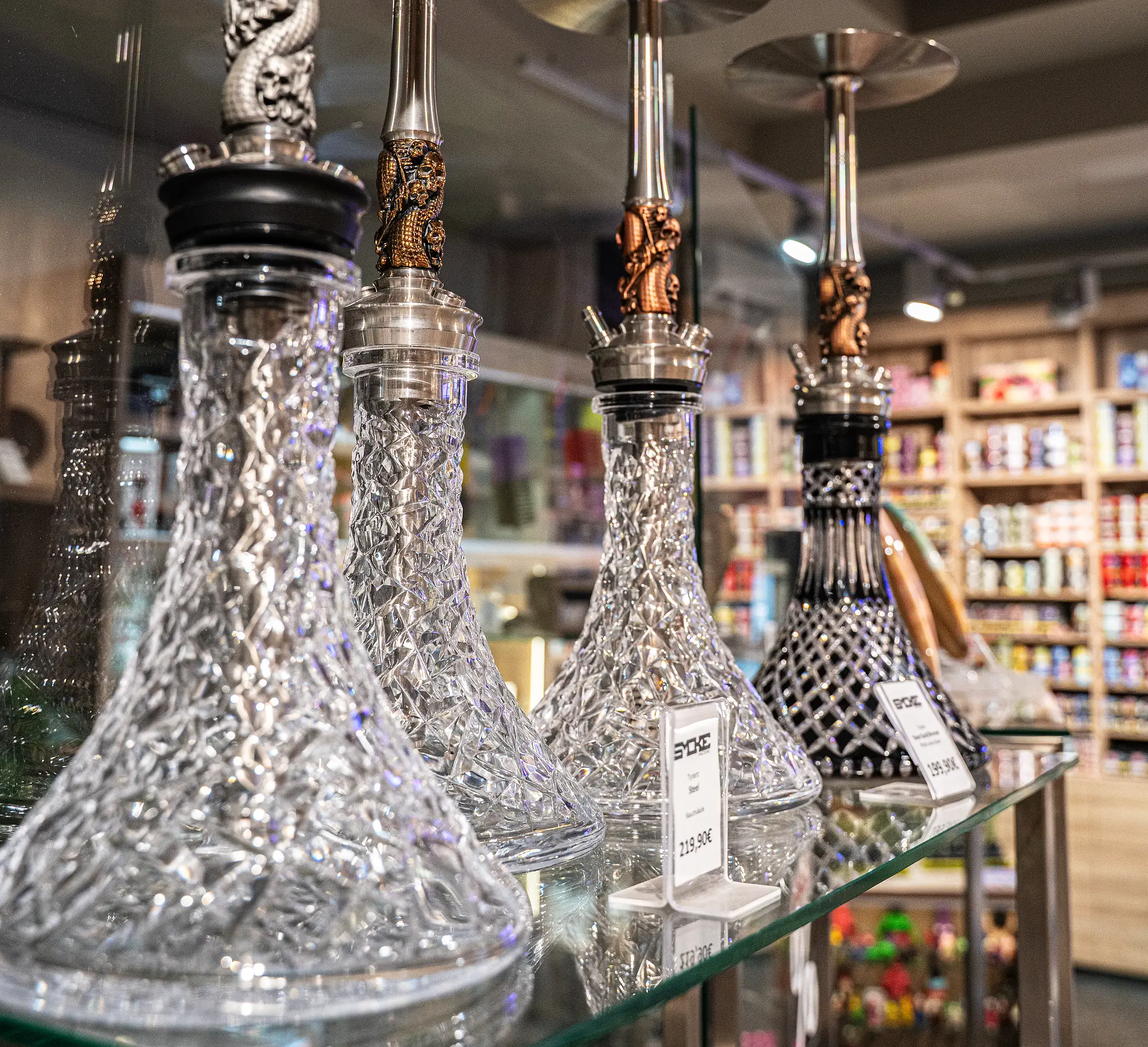 SYCKE Kristall-Shishas mit goldenen Drachen-Verzierungen in der Glasvitrine bei SmokeFactory Köln