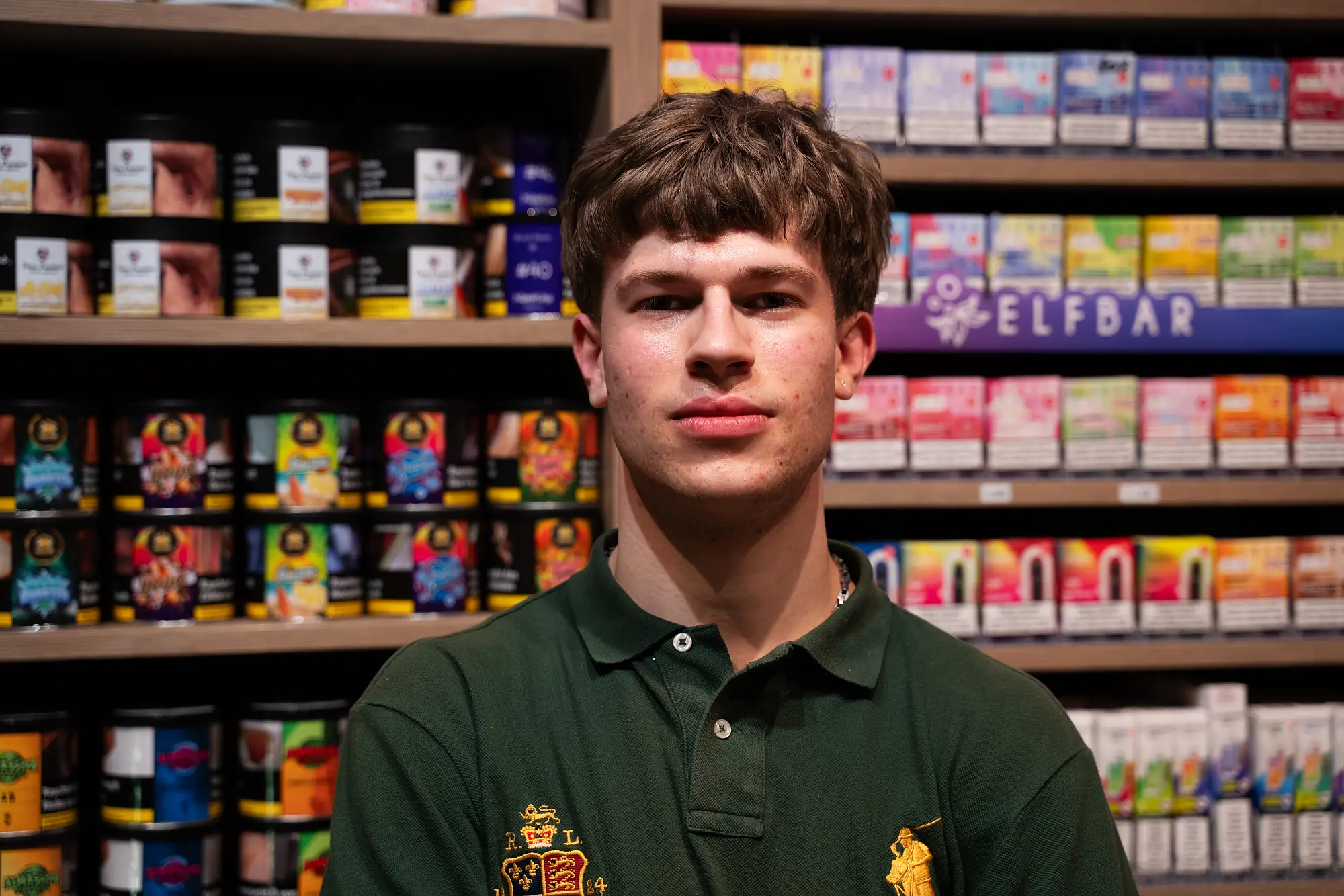 Mitarbeiter von SmokeFactory Köln im grünen Poloshirt vor dem Geräte- und Tabakregal