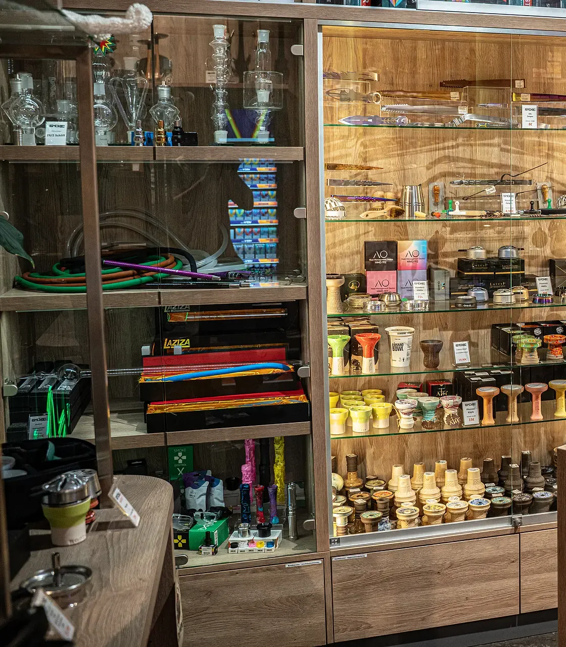 Beleuchtete Vitrine mit Shisha-Zubehör, Kohlezangen und bunten Köpfen bei SmokeFactory Köln